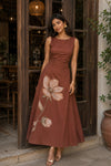 Woman wearing a Brown-colored Sakshyaa dress with Hand-painted flowers standing in front of a wooden door.
